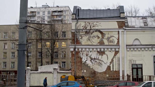 Ein großes Porträt mit Brille ist auf eine Hauswand gemalt.