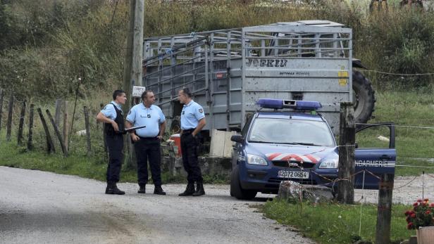 Drei Gendarmen stehen neben einem Gendarmerie-Fahrzeug und einem Anhänger auf einer Landstraße.
