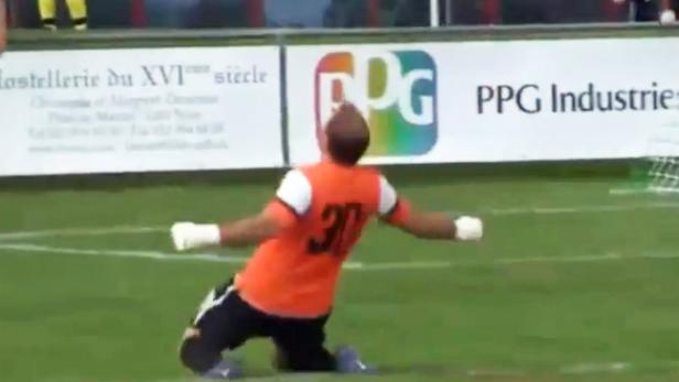 Ein Torwart kniet auf dem Rasen und jubelt mit ausgestreckten Armen.