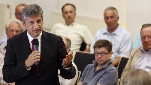 Ein Mann im Anzug spricht vor einer Gruppe von Zuhörern in ein Mikrofon.