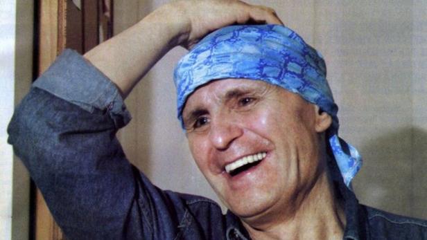 Ein lächelnder Mann mit blauem Kopftuch und Jeanshemd.