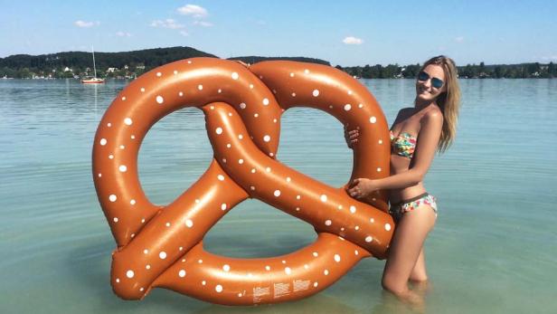 Eine Frau im Bikini posiert mit einer riesigen Brezel-Luftmatratze im Wasser.