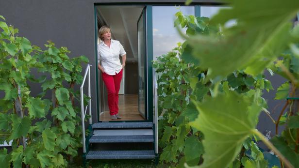 Eine Frau in roter Hose steht in einer Haustür, umgeben von Weinreben.