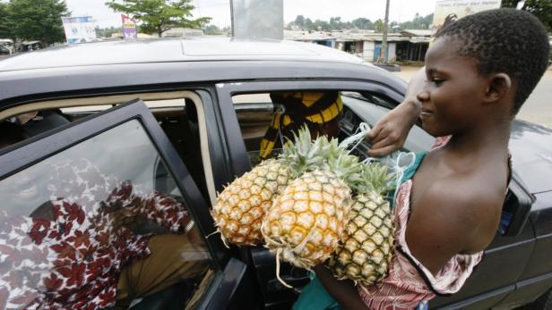 Ein junges Mädchen verkauft Ananas an die Insassen eines Autos.