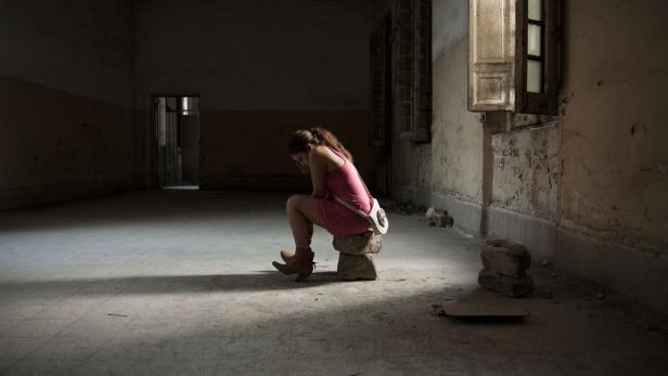 Eine junge Frau sitzt in einem verlassenen Raum auf einem Stapel Steine.