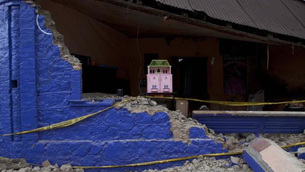 Ein zerstörtes Haus mit einer pinkfarbenen Puppenstube davor, umgeben von Absperrband.