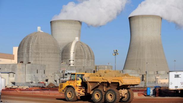 Ein gelber Muldenkipper vor einem Atomkraftwerk mit Kühltürmen.
