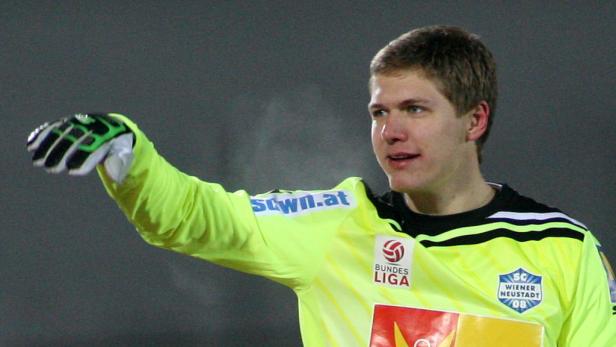Ein Torwart in gelber Sportkleidung mit Handschuhen streckt den Arm aus.