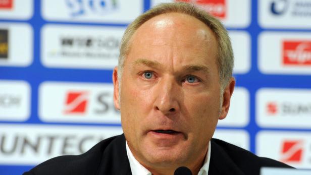 Ein Mann mit hellblauen Augen spricht in ein Mikrofon vor einer Sponsorenwand.