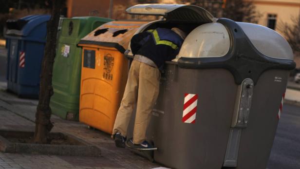 Eine Person sucht in einem Müllcontainer nach etwas Brauchbarem.