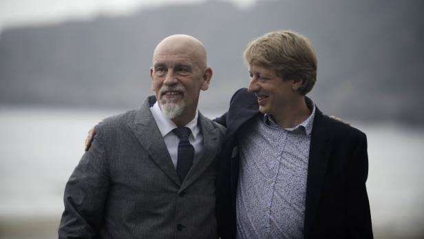 John Malkovich und ein Mann stehen im Anzug nebeneinander.