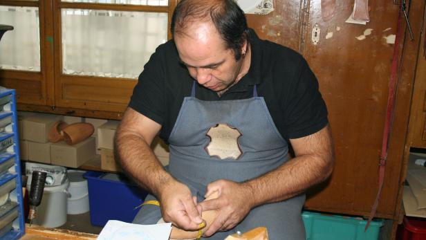 Ein Schuhmacher misst einen Holzschuhleisten mit einem gelben Maßband.