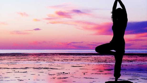 Eine Frau macht Yoga am Strand bei Sonnenuntergang.