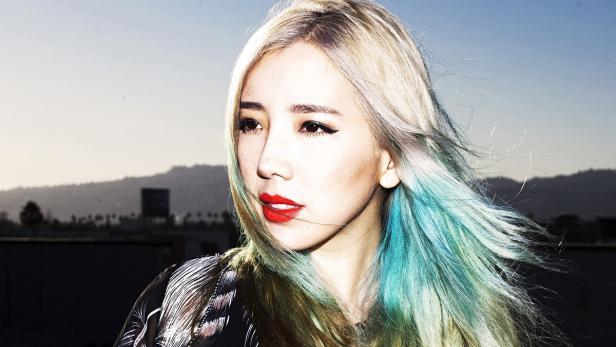 Eine Frau mit blond gefärbten Haaren und türkisfarbenen Spitzen blickt nach links.