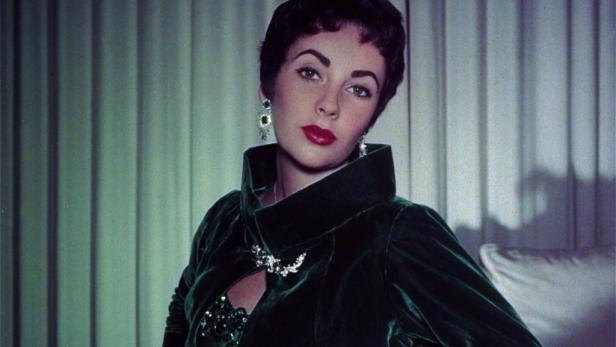 Elizabeth Taylor trägt ein grünes Samtkleid und auffälligen Schmuck.