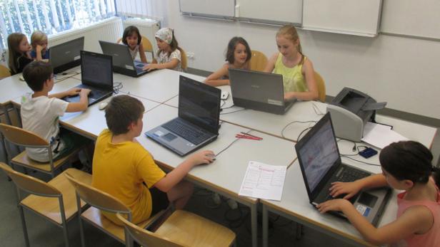 Eine Gruppe von Kindern sitzt an einem Tisch und benutzt Laptops.