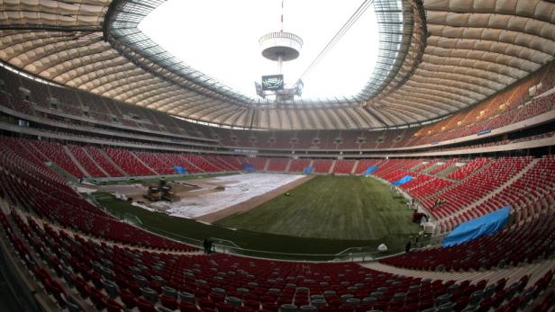 Blick in das Innere des Nationalstadions Warschau mit roten Sitzen und teilweise abgedecktem Rasen.