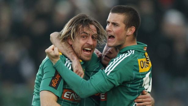 Drei Fußballspieler in grünen Trikots umarmen sich und jubeln.