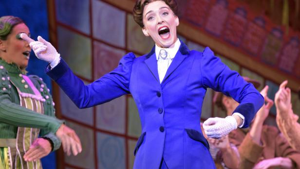 Eine Schauspielerin in einem blauen Kostüm singt auf einer Bühne.