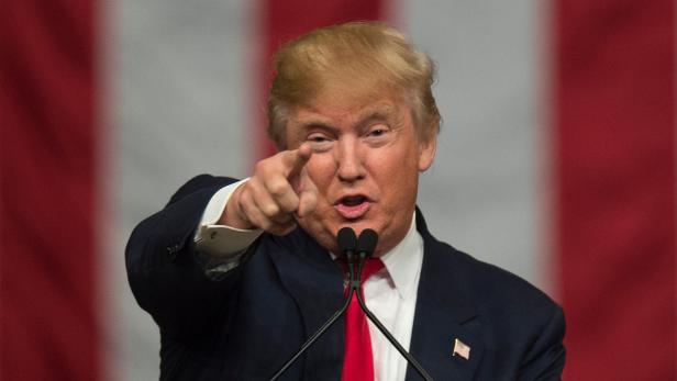 Donald Trump gestikuliert bei einer Rede vor einer rot-weiß gestreiften Flagge.