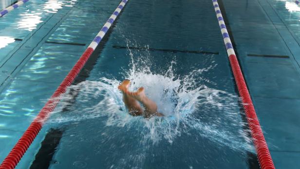 Ein Schwimmer springt ins Wasser eines Schwimmbeckens.