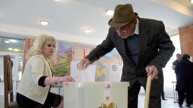 Ein älterer Mann mit Hut wirft seinen Stimmzettel in eine Wahlurne.