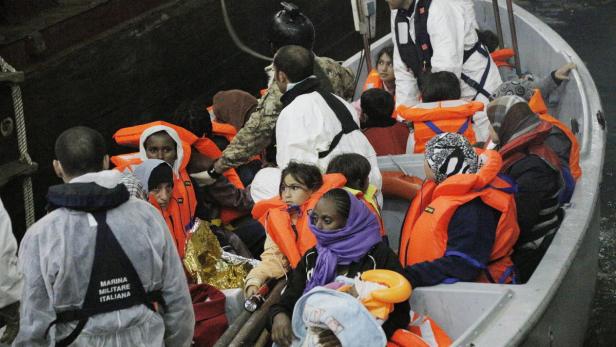 Ein Boot voller Menschen, darunter Kinder, trägt orangefarbene Schwimmwesten.