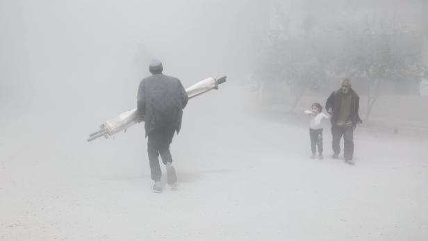 Ein Mann trägt eine Rolle durch dichten Nebel, während ein älterer Mann mit einem Kind an der Hand geht.