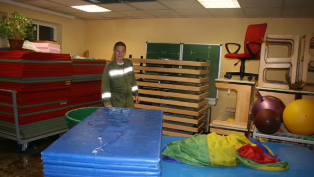 Ein Mann in Arbeitskleidung steht in einem Raum voller Sportgeräte und Matten.