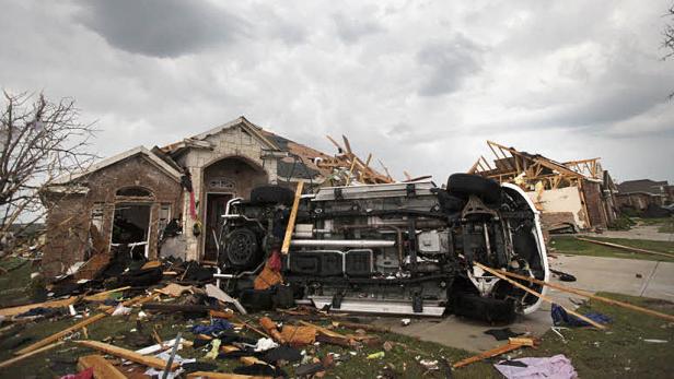 Ein umgekipptes Auto liegt vor einem durch einen Sturm beschädigten Haus.