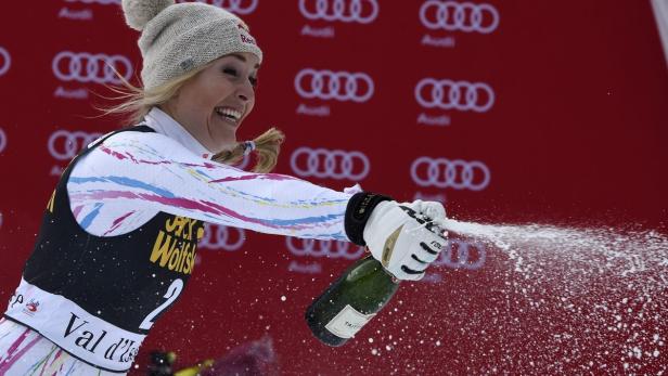 Eine Skirennläuferin feiert mit einer Champagnerflasche vor einem roten Audi-Hintergrund.