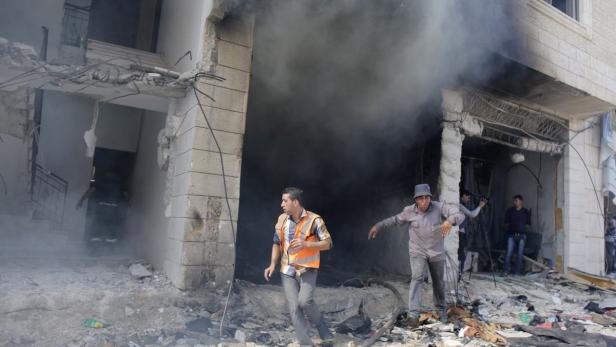 Menschen fliehen aus einem zerstörten Gebäude, aus dem Rauch dringt.