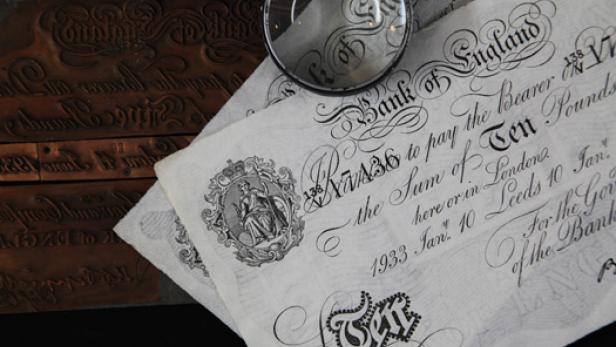 Eine Lupe liegt auf zwei alten Zehn-Pfund-Banknoten der Bank of England von 1933.