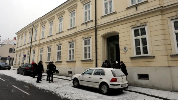 Vor einem Gebäude stehen Menschen und Autos im winterlichen Wien.
