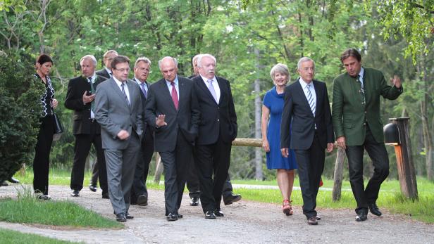 Eine Gruppe von Menschen geht auf einem Weg durch eine parkähnliche Anlage.