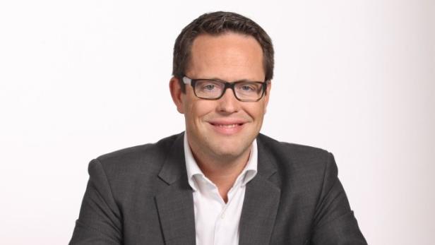 Ein Mann mit Brille und grauem Sakko lächelt in die Kamera.