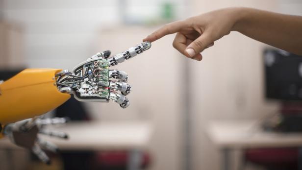 Eine Roboter-Hand und eine menschliche Hand berühren gegenseitig ihren Zeigefinger