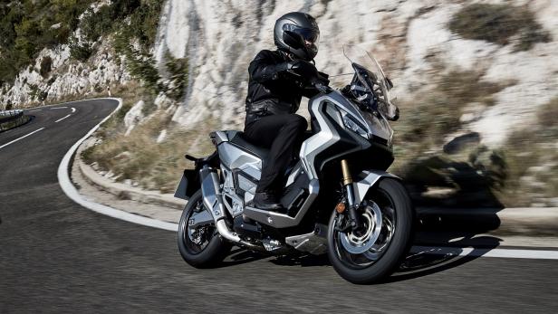 Ein Motorradfahrer fährt auf einer kurvenreichen Straße entlang einer Felswand.
