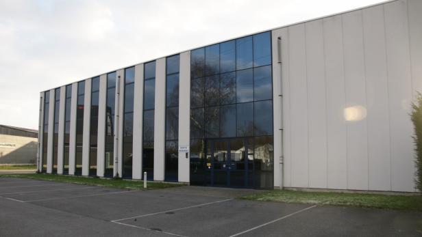 Ein modernes Bürogebäude mit blauen Glasfenstern und einem Parkplatz davor.