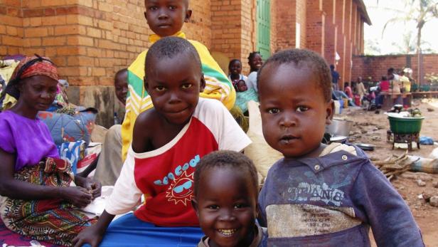 Eine Gruppe afrikanischer Kinder posiert vor einem Backsteingebäude.