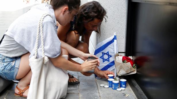 Zwei Frauen zünden Kerzen vor einer israelischen Flagge und einem Blumenstrauß an.