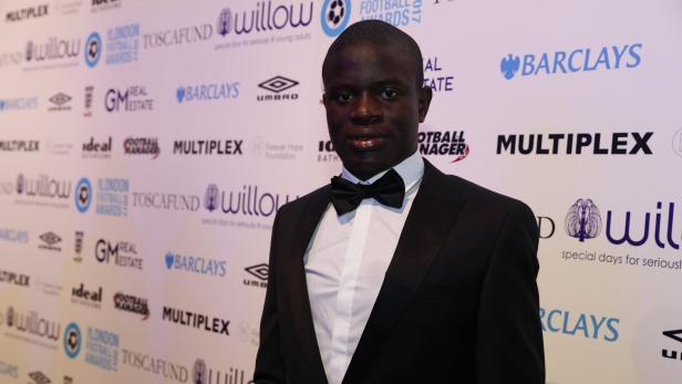 N'Golo Kanté in einem schwarzen Smoking mit Fliege vor einer Wand mit Sponsorenlogos.