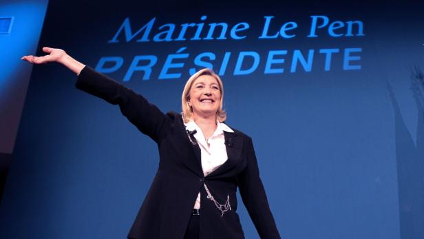 Marine Le Pen posiert vor einem blauen Hintergrund mit der Aufschrift „Marine Le Pen Présidente“.
