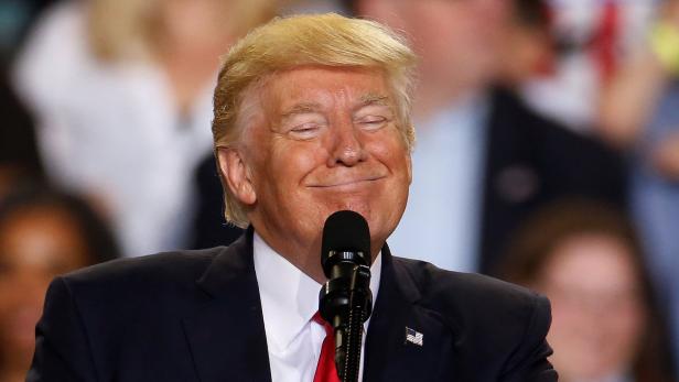 Donald Trump lächelt mit geschlossenen Augen vor einem Mikrofon.