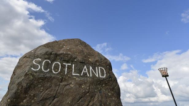 Ein großer Stein mit der Aufschrift „Scotland“ vor blauem Himmel.