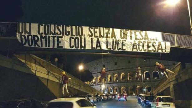 Über einer Straße in Rom hängt ein Banner mit der Aufschrift „Ein Rat, ohne Beleidigung... Schlaft mit dem Licht an!“.