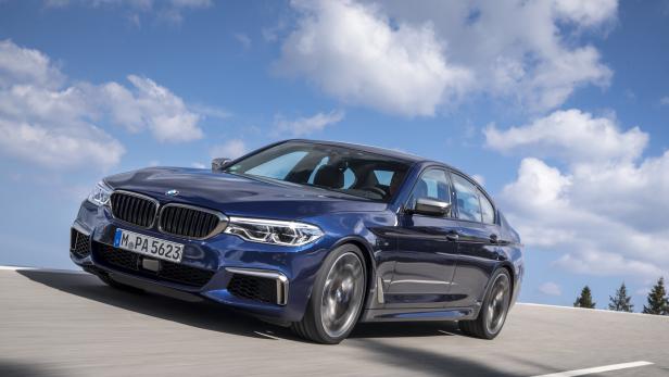 Ein blauer BMW der 5er-Reihe fährt auf einer Straße unter blauem Himmel.