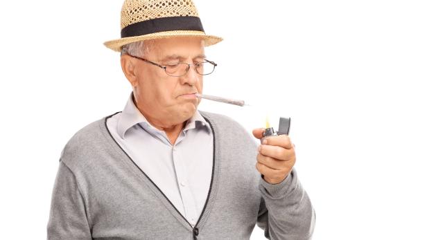 Ein alter Mann mit Hut zündet sich mit einem Feuerzeug einen Joint an