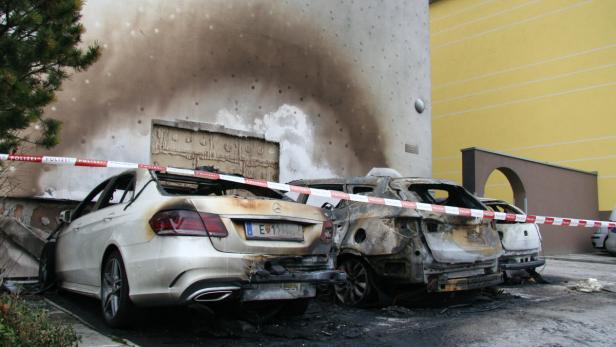Mehrere ausgebrannte Autos stehen vor einem Gebäude, abgesperrt mit einem rot-weißen Polizeiband.