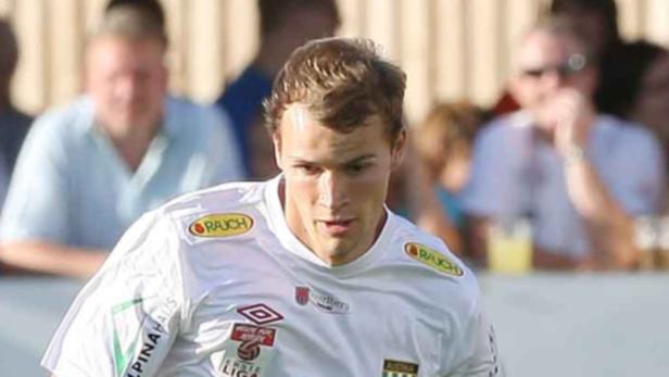 Ein Fußballspieler im weißen Trikot mit dem Logo des Sponsors „Rauch“.